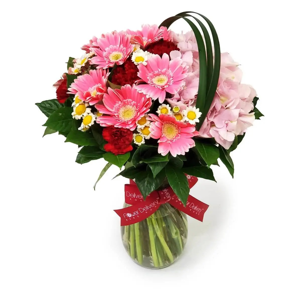Pink gerberas, red carnations, pale pink hydrangeas, and chamomile flowers with greenery in a glass vase. 粉紅太陽菊、紅康乃馨、淺粉繡球花及洋甘菊,搭配綠葉插於玻璃瓶中。
