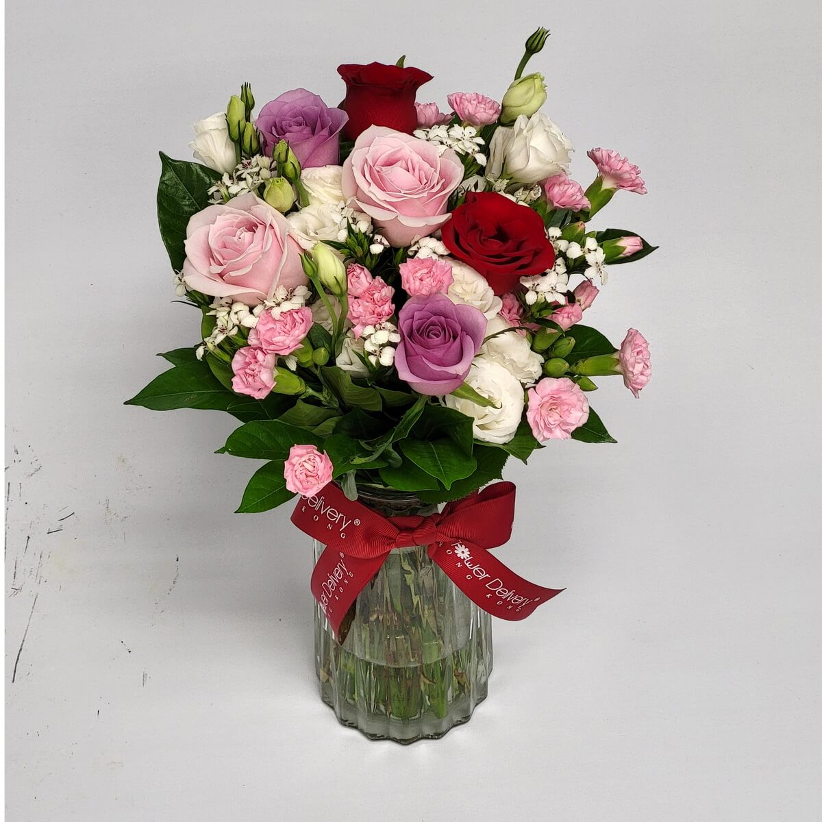 Elegant bouquet of roses in red, pink, lavender, and white with pink carnations and greenery 紅、粉、紫、白玫瑰配粉康乃馨與綠葉,置於玻璃瓶中,優雅脫俗。