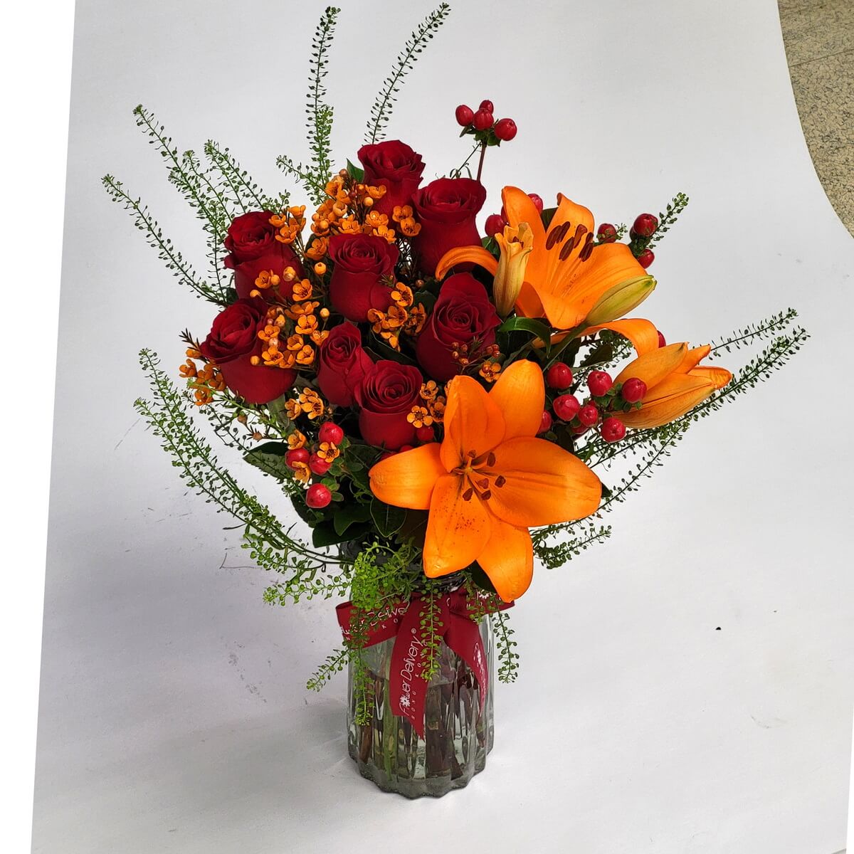 Glass vase floral arrangement featuring red roses, vivid orange lilies, red berries, and yellow filler blooms with greenery - 紅玫瑰、橙百合、紅漿果與黃色小花綠葉玻璃瓶插花
