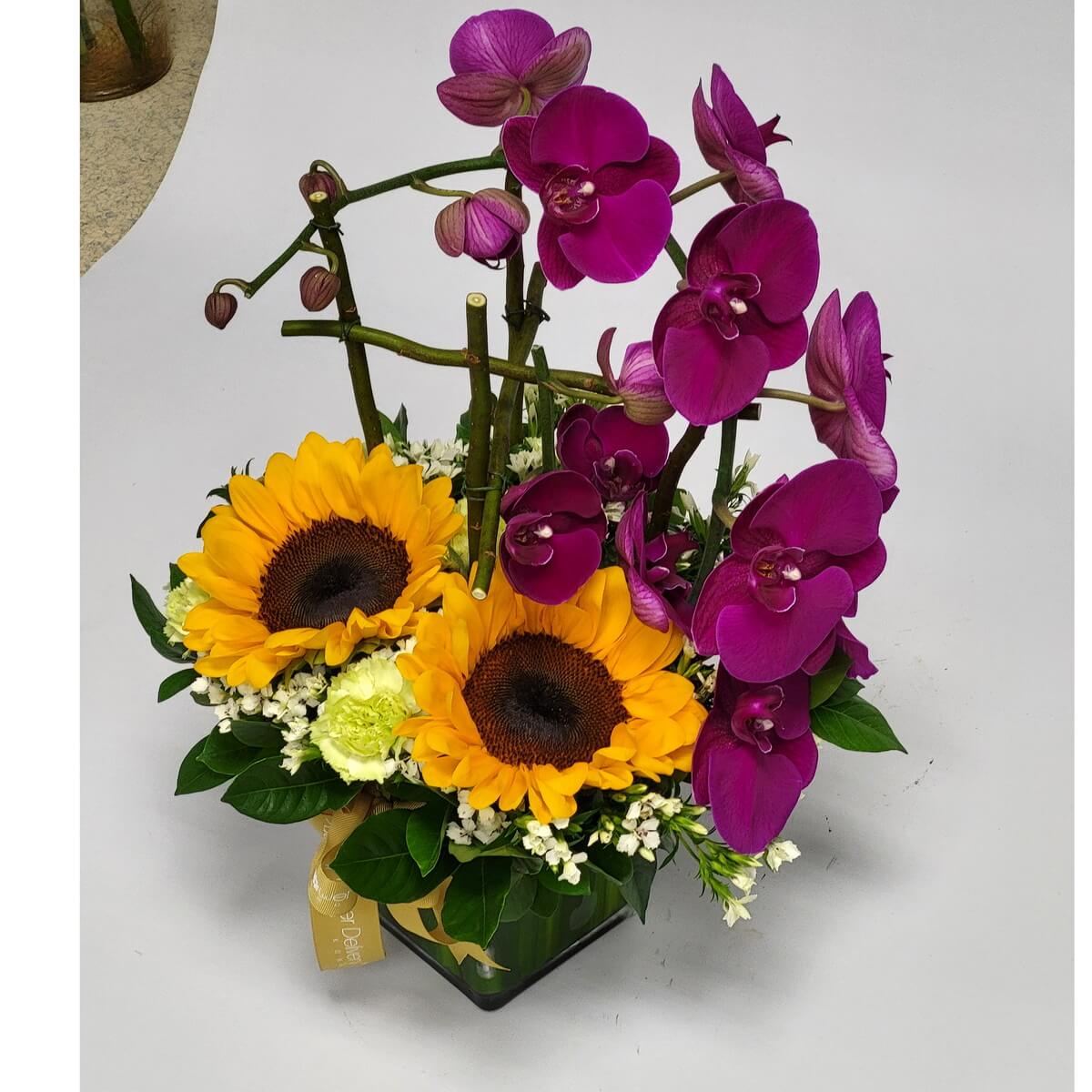 Contemporary square glass vase featuring cascading purple orchids, sunflowers, green carnations, and clusters of white dianthus 現代方玻璃瓶設計,搭配垂落紫蝴蝶蘭、向日葵、綠康乃馨與白石竹花