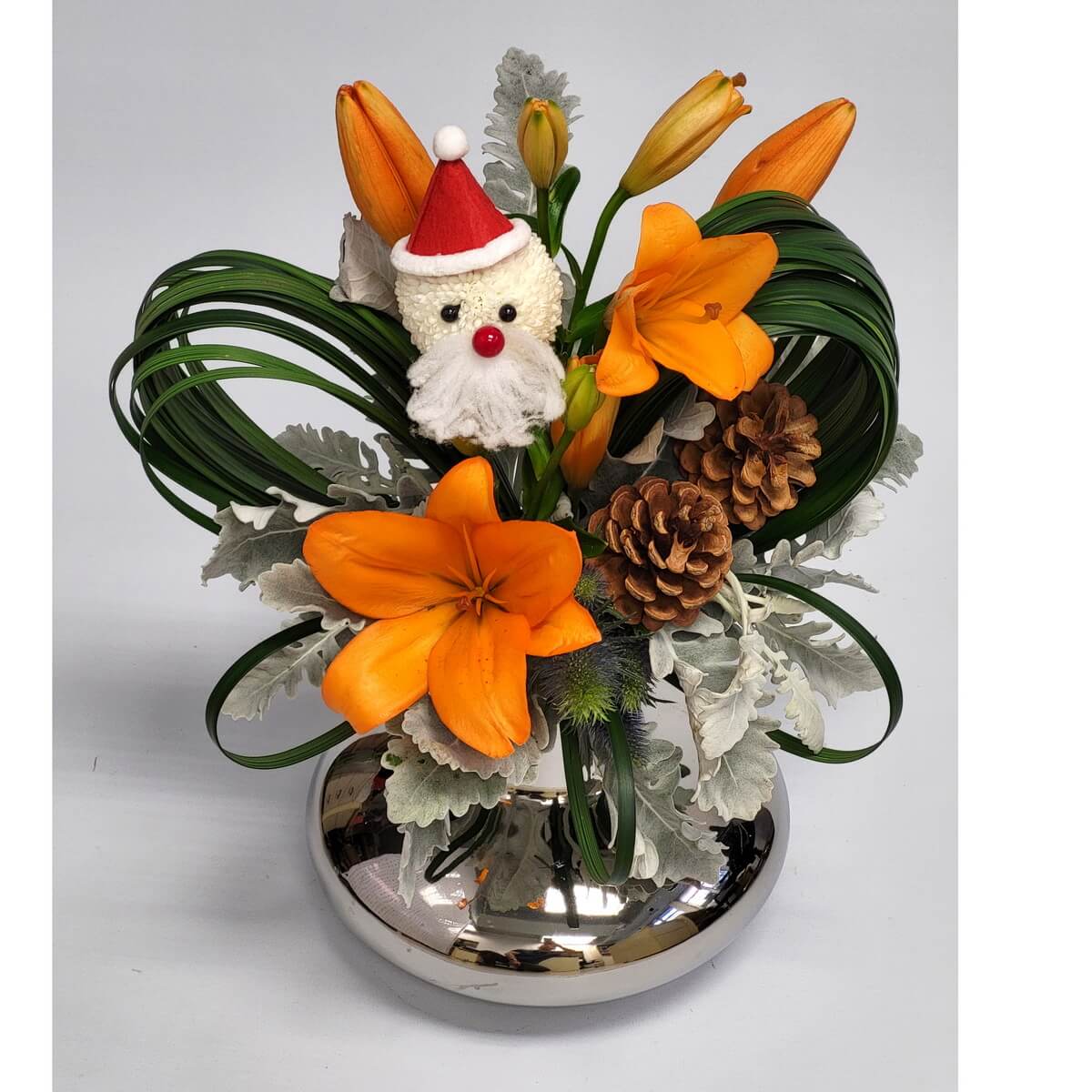 Original image of festive silver vase arrangement with Santa face made from white button chrysanthemums, paired with orange Asiatic lilies, pinecones, dusty miller, green loops, and eryngium - 銀瓶節日插花配白乒乓菊製聖誕老人、橙百合、松果、銀葉菊、彎葉與藍刺芹裝飾