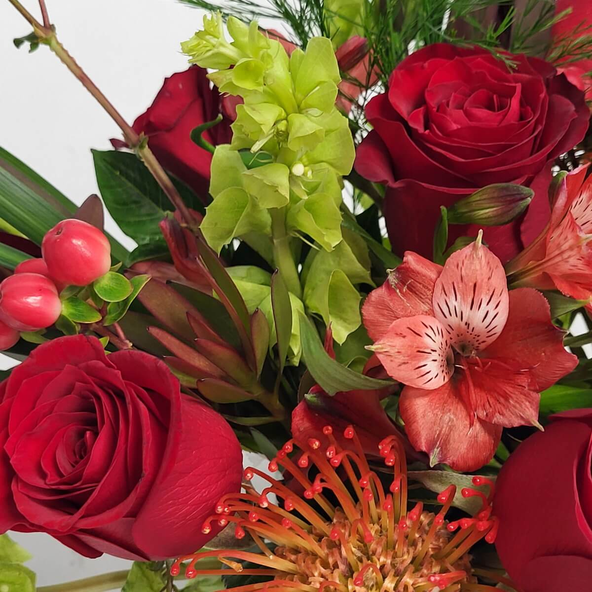Close-up featuring red roses, coral alstroemeria, orange pincushion protea, green bells of Ireland, and red hypericum berries - 花藝特寫含紅玫瑰、橘紅金魚花、橙針墊花、綠愛爾蘭鈴與紅繡球果