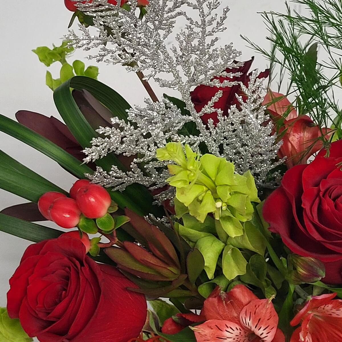 Close-up of floral mix with red roses, coral alstroemeria, green bells of Ireland, red hypericum berries, and glittered silver foliage - 花藝特寫含紅玫瑰、珊瑚金魚花、愛爾蘭鈴、紅繡球果與銀粉葉材
