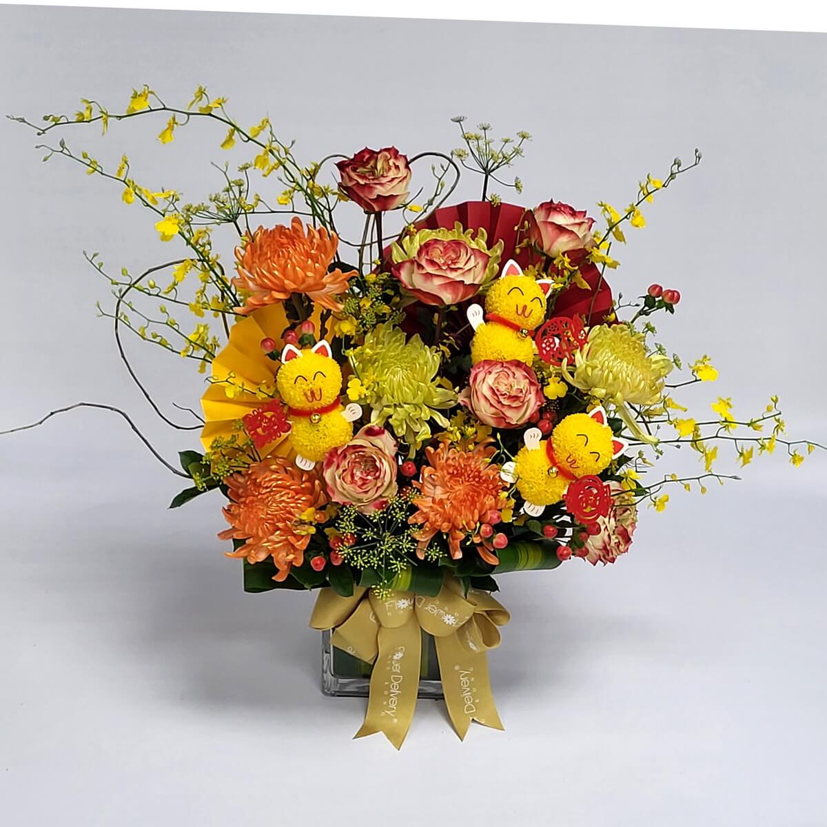 Arrangement of chrysanthemums, bicolor roses, oncidium orchids, berries, red-yellow paper fans, and cat decorations in a glass vase 橙黃菊花搭配雙色玫瑰、舞春蘭、紅色漿果、紅黃摺紙扇及黃色招財貓擺件,插於玻璃花瓶中,造型豐富熱鬧。