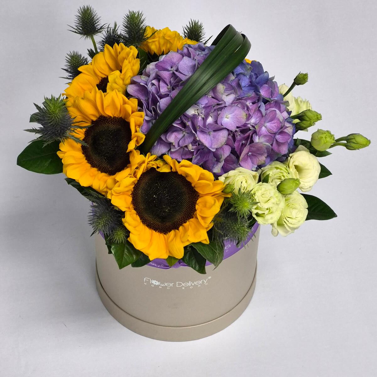Real photo of hat box flower arrangement with yellow sunflowers, purple hydrangea and white lisianthus with green foliage - 向日葵、紫色繡球花與白色洋桔梗帽盒花藝配綠葉