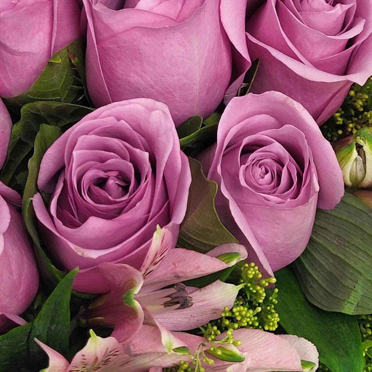 Zoomed-in floral detail of lavender roses and soft pink alstroemeria framed with dense greenery and textured leaves - 紫玫瑰與粉色百合配綠葉與紋理葉片花藝細節特寫