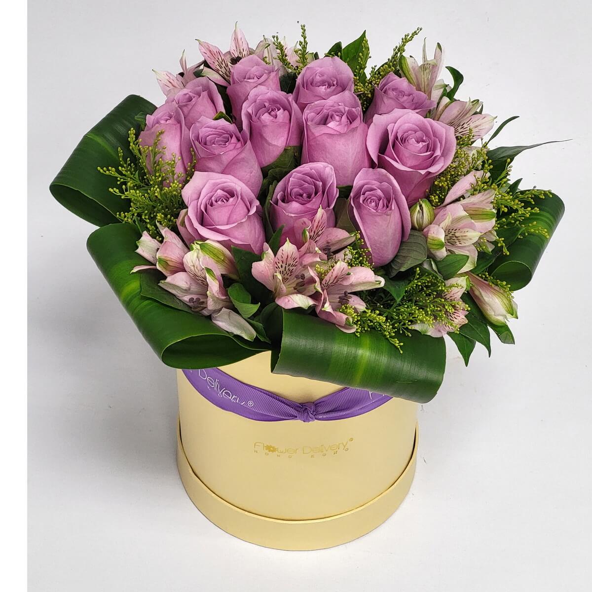 Full arrangement of lavender roses and pink alstroemeria with folded tropical leaves and yellow fillers in a cream round hat box - 紫玫瑰與粉百合配摺葉和黃色配花的奶油色圓形花盒花藝