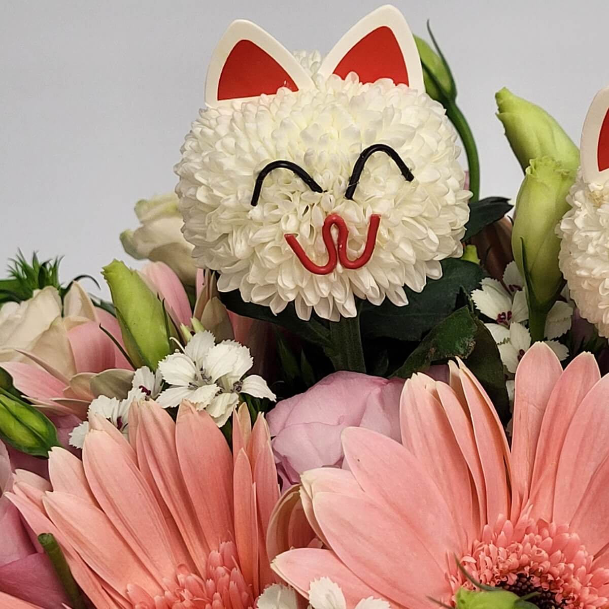 Close-up of playful cat-faced white button chrysanthemums with pink gerberas, lisianthus buds, and dianthus 仿貓咪臉設計的白色乒乓菊,周圍有粉紅非洲菊、洋桔梗花苞及白色石竹,整體色彩柔和。