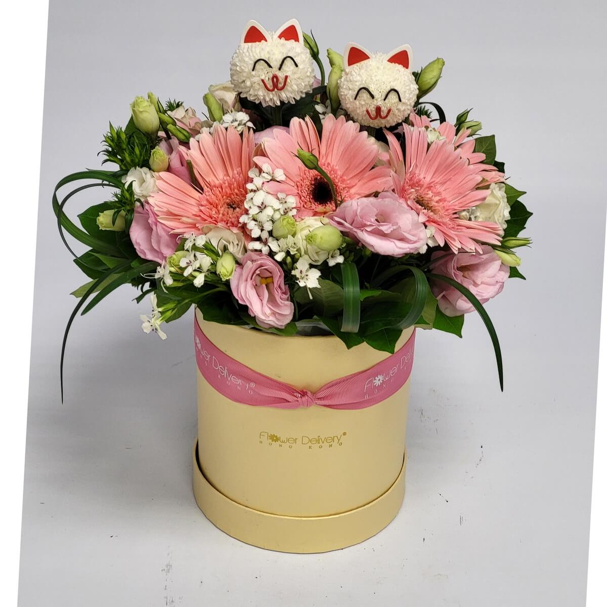 Floral box with pink gerberas, lisianthus, white filler flowers, assorted greenery, and two cat decorations 粉紅非洲菊與洋桔梗組合,配白色配花與多款綠葉,花盒中另飾有兩個貓咪擺件設計。