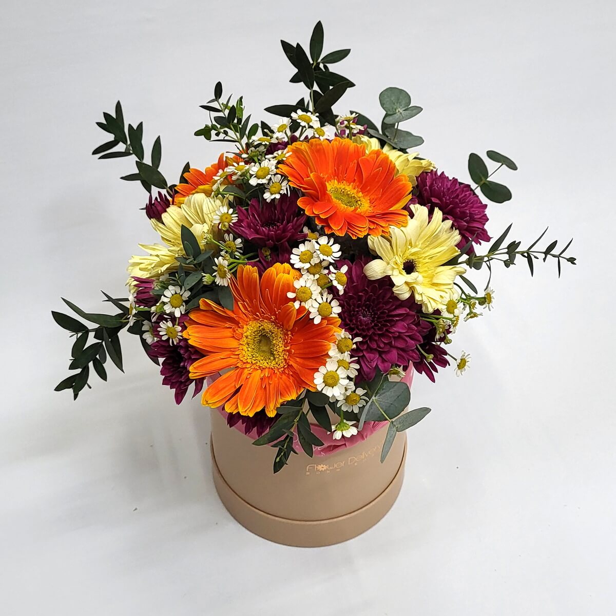 Floral hatbox featuring orange gerberas, pale yellow and burgundy chrysanthemums, chamomile flowers, and eucalyptus foliage 圓形花盒設計,橙色非洲菊配淡黃及酒紅色菊花、洋甘菊與尤加利葉,色彩豐富。