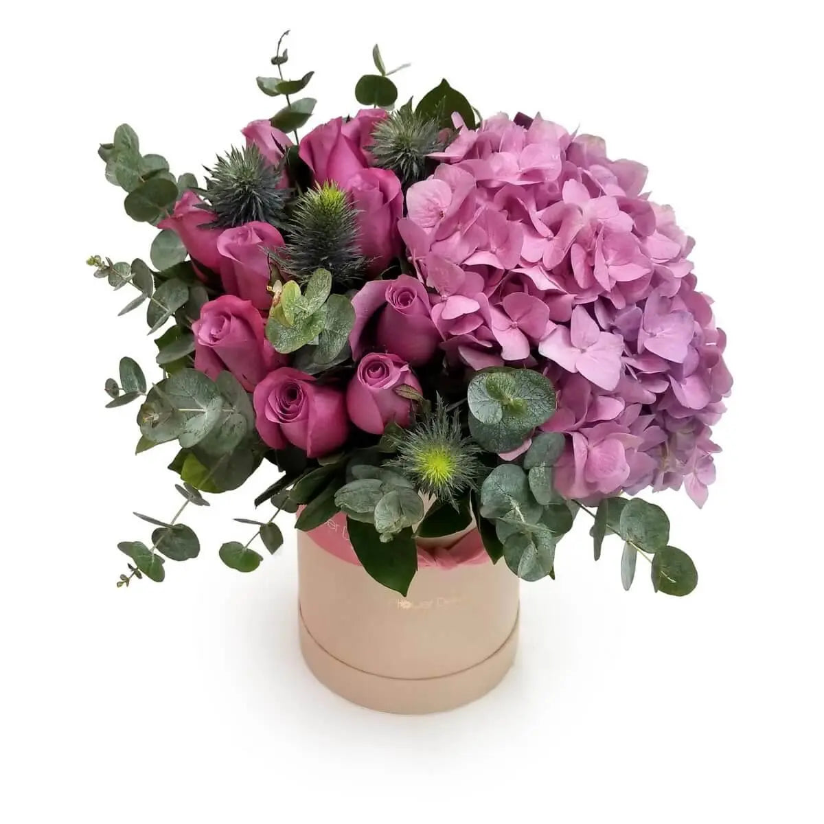 Mauve roses, pink hydrangeas, blue thistles, and eucalyptus foliage in a beige round box arrangement. | 紫玫瑰、粉紅繡球花、藍刺頭及尤加利葉搭配米色圓形花盒設計。