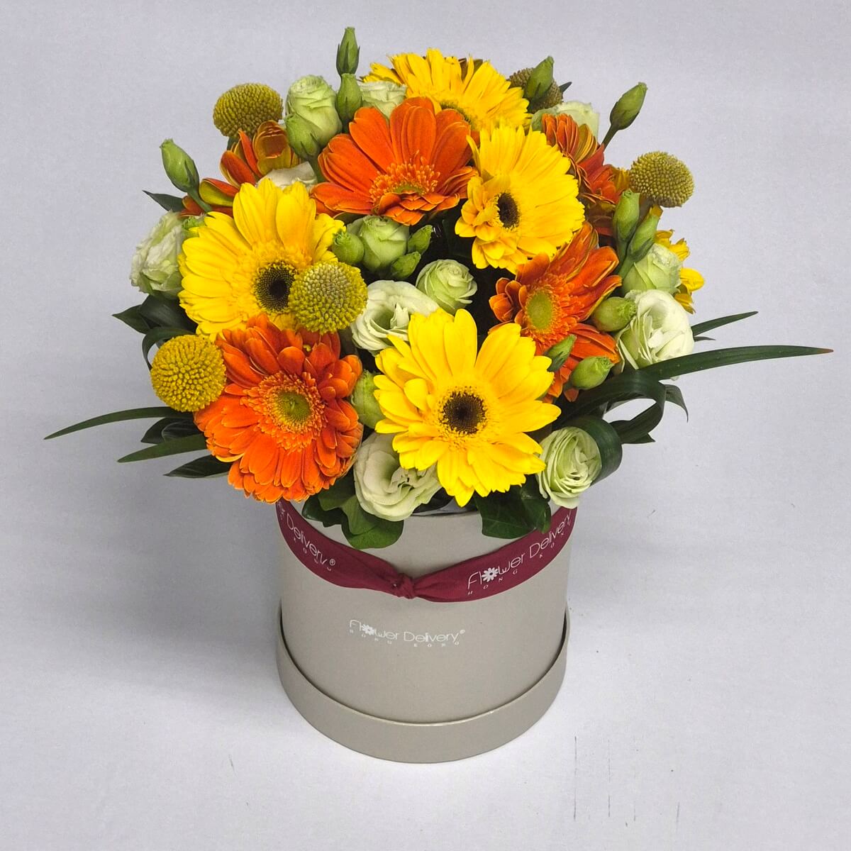 Original photo of round hatbox floral arrangement featuring yellow and orange gerbera daisies, white lisianthus and button chrysanthemums with green foliage - 黃橙色扶郎花配白色洋桔梗、乒乓菊及綠葉圓帽盒花藝設計