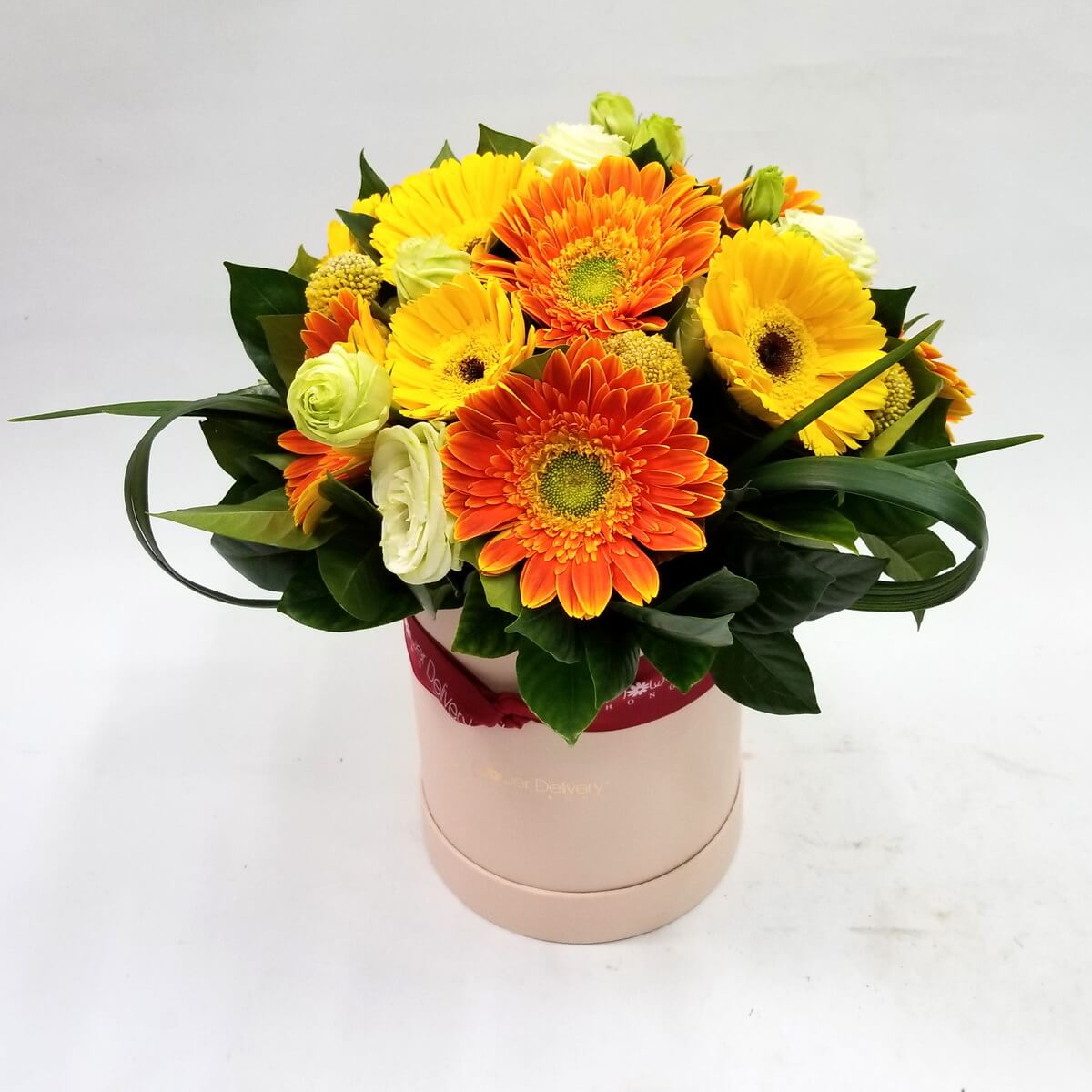 Floral box with orange and yellow gerberas, white roses, button chrysanthemums, and greenery 圓形花盒擺設,橙黃非洲菊配白玫瑰、小乒乓菊及多款綠葉,色彩鮮明。