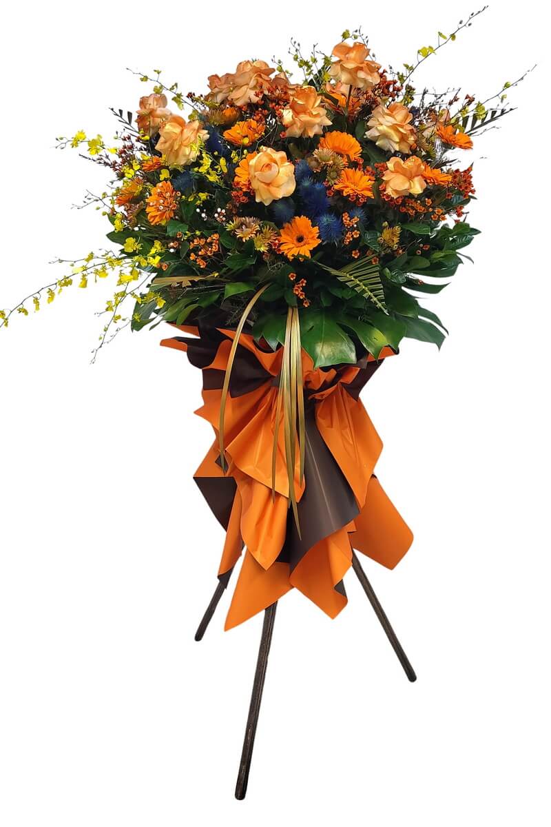 Full standing spray featuring orange roses, gerberas, yellow oncidium orchids, blue thistles, and assorted fillers with lush foliage and orange-brown wrapping - 橙玫瑰太陽菊黃文心蘭藍薊與豐富配花配橙啡包裝企牌花籃