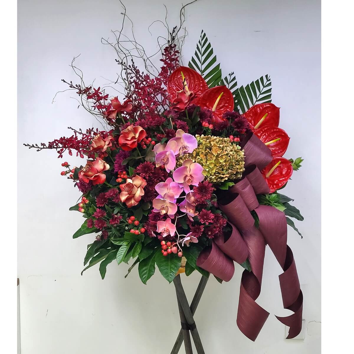A luxurious grand opening stand featuring red anthuriums, burgundy orchids, pink phalaenopsis, and bronze roses. 鮮紅火鶴、紅酒色蘭花與粉蝴蝶蘭交織,呈現高貴喜慶氣氛。