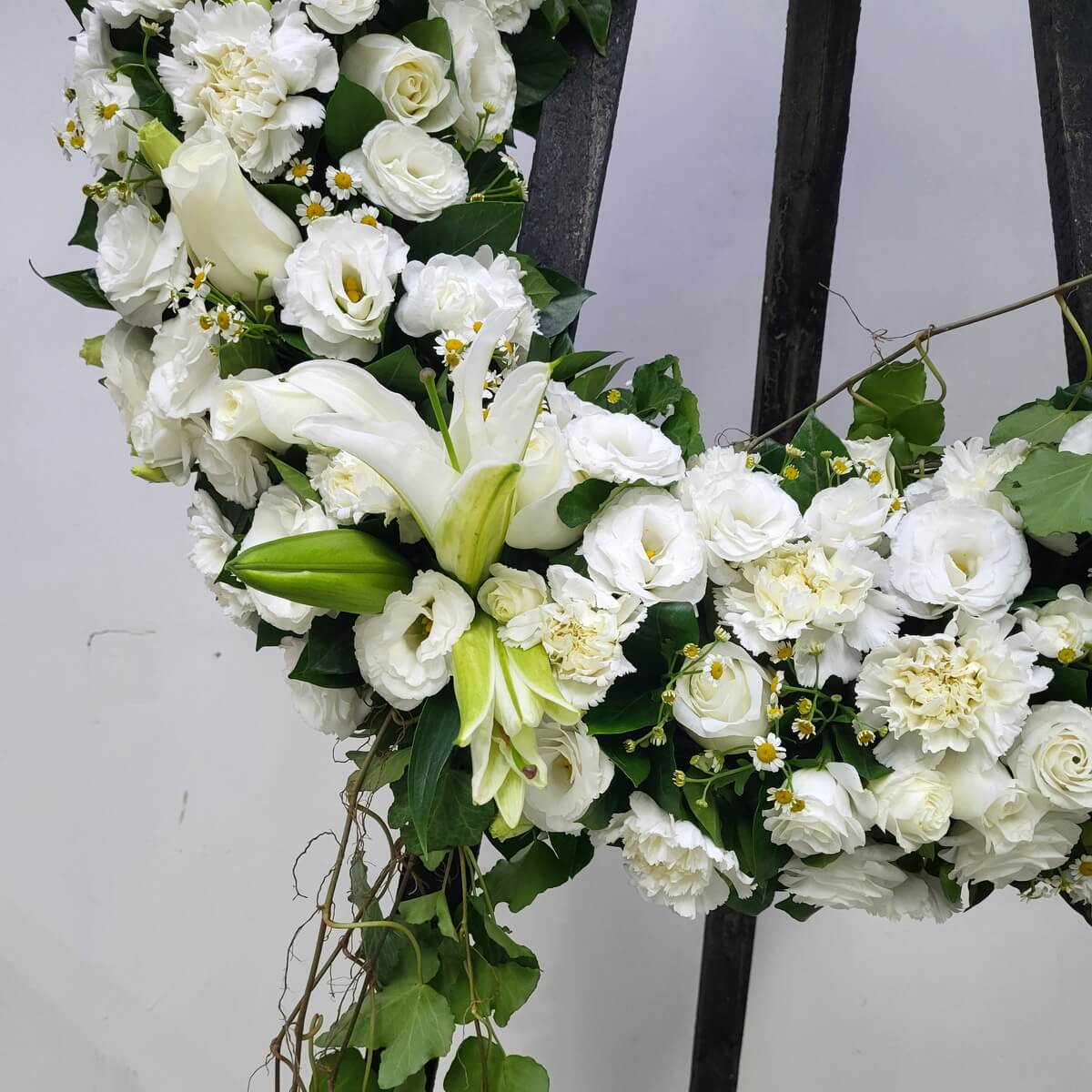 Zoomed-in view showing white lilies, roses, lisianthus, carnations, small yellow-centered daisies, and cascading ivy from floral wreath - 白百合、玫瑰、洋桔梗、康乃馨、黃芯小白菊及垂藤花圈局部放大圖