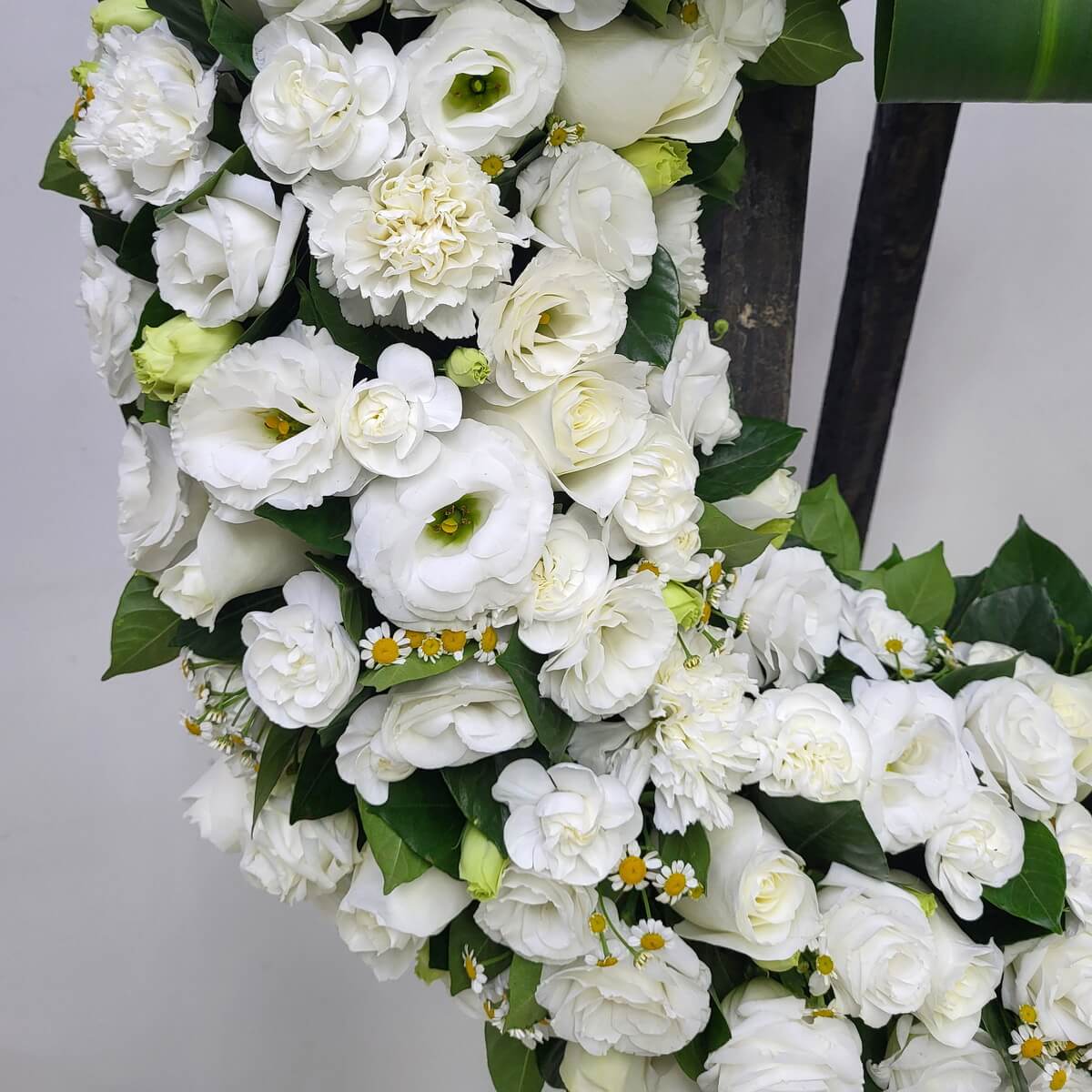 Close-up of wreath segment with white lisianthus, roses, carnations, yellow-centered chamomile daisies and dark green foliage - 花圈局部特寫:白洋桔梗、玫瑰、康乃馨、黃芯小白菊及深綠葉片花材組合