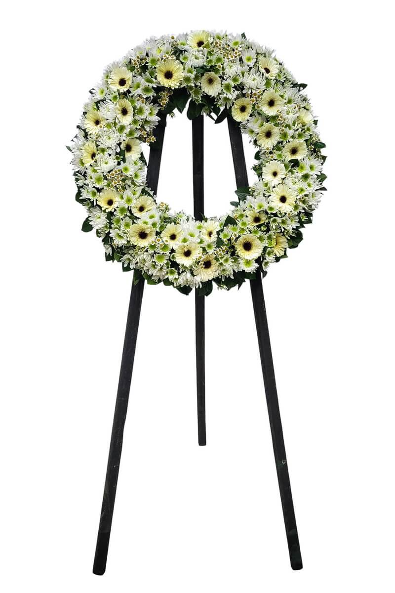 Full wreath of white and pale yellow gerberas with mixed white chrysanthemums including green-centered blooms, arranged with foliage on a black easel - 白色及淡黃色太陽菊配混合綠芯白菊花材圓形花圈加綠葉設計擺放於黑色支架上