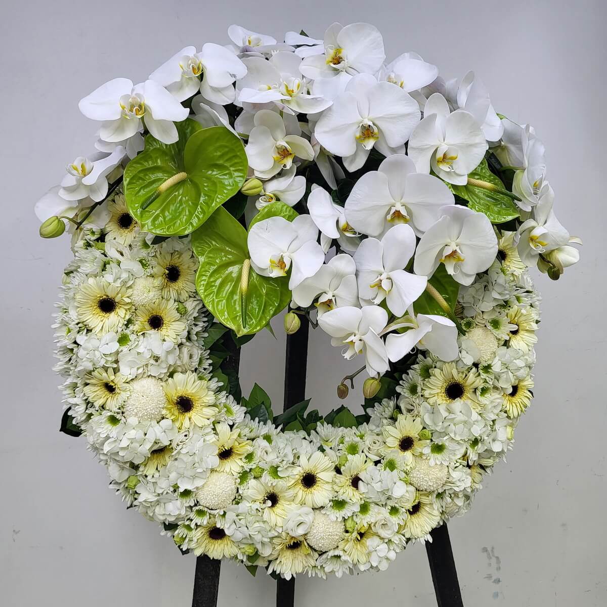 Complete standing floral wreath featuring cascading white phalaenopsis orchids and green anthuriums, set over a circular base of white gerberas, button chrysanthemums, and hydrangeas 垂墜式白色蝴蝶蘭與綠色火鶴花,搭配白色非洲菊、乒乓菊及繡球花圓形立式花圈設計