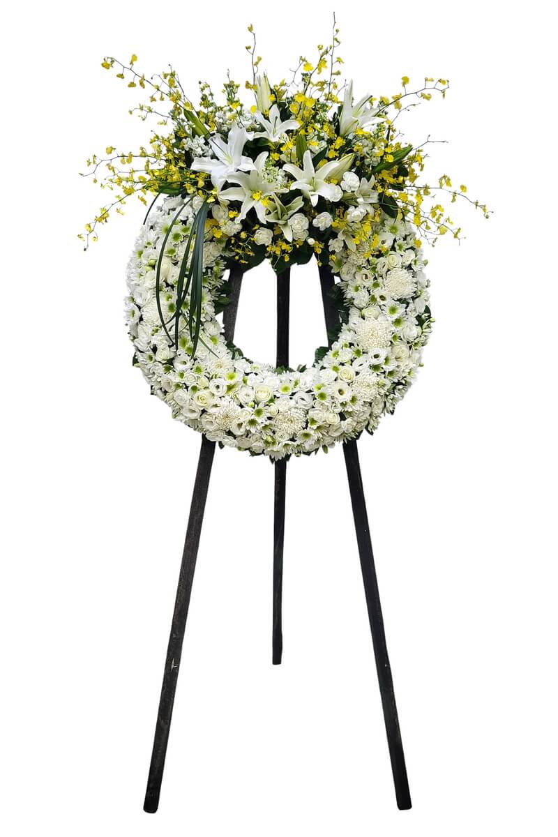 Standing circular wreath with cascading white lilies and yellow dancing orchids above a floral base of white roses, button chrysanthemums, spray carnations, and filler greens 白色百合與黃色跳舞蘭垂墜設計,搭配白玫瑰、乒乓菊、迷你康乃馨與綠葉素材的圓形立式花圈