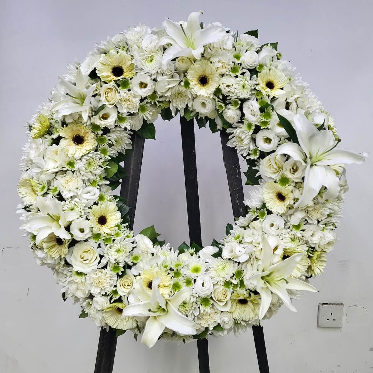 Round floral wreath featuring white lilies, cream gerberas, ivory roses, lisianthus, and button chrysanthemums with green foliage - 白百合、奶白非洲菊、象牙白玫瑰、洋桔梗及乒乓菊搭配綠葉花圈