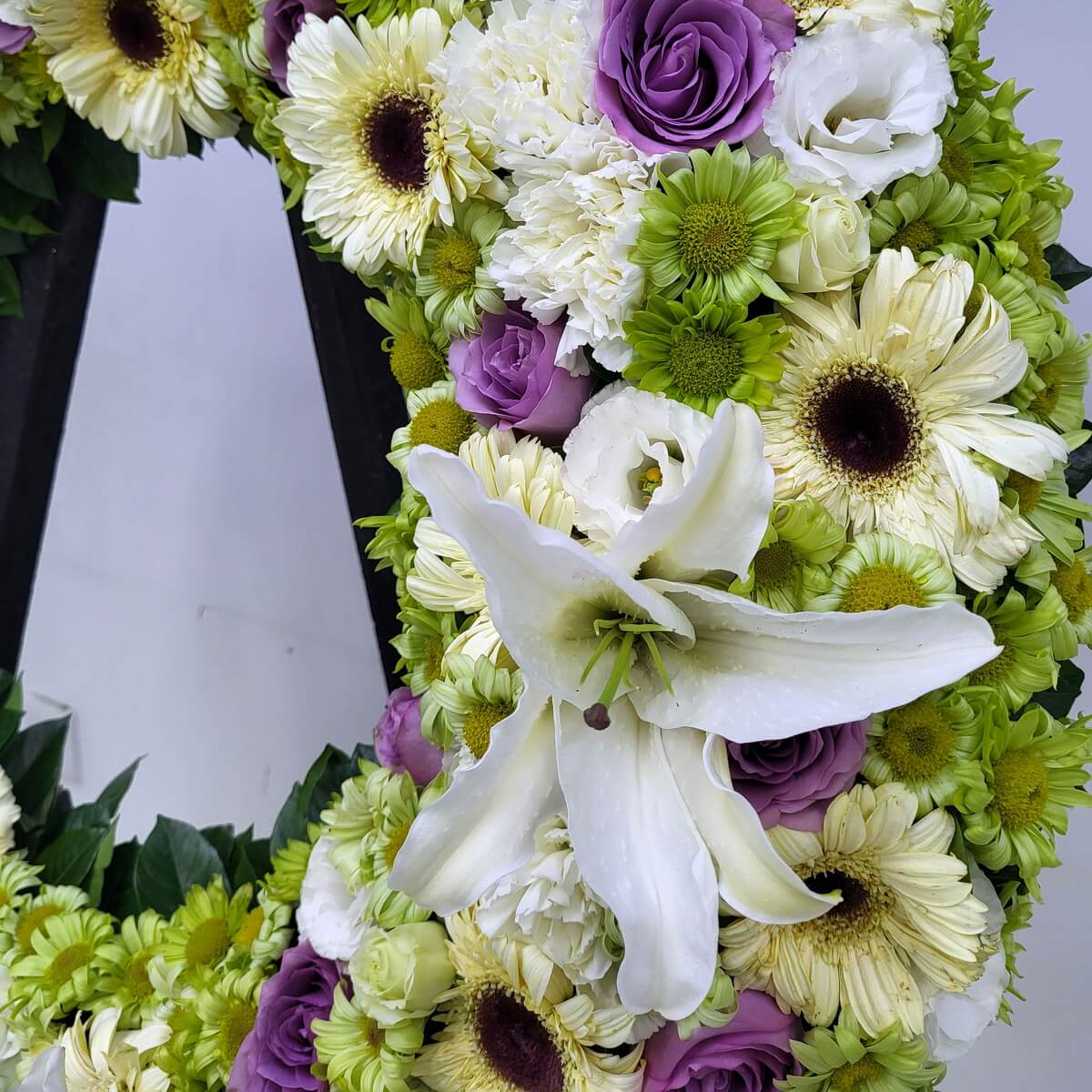 Close-up view of a circular wreath section featuring white gerbera daisies, white lilies, white lisianthus, green button chrysanthemums, and purple roses 花圈局部近距離細節-白色非洲菊、百合、洋桔梗、綠菊花及紫玫瑰