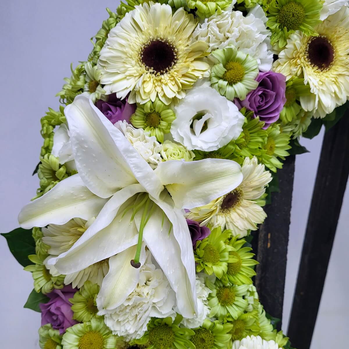 Close-up of a floral wreath section with white gerbera daisies, white lilies, green button chrysanthemums, white lisianthus, and purple roses 花圈近距離細節-白色非洲菊、百合、洋桔梗、綠色菊花及紫色玫瑰