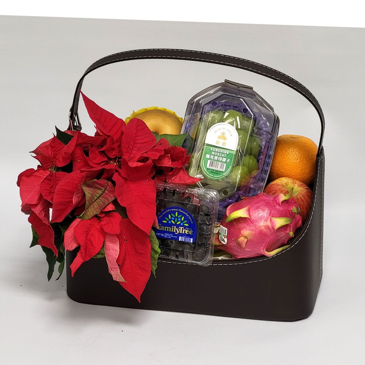 Festive fruit basket featuring red poinsettia 聖誕紅與新鮮水果組合,內含黑莓、青葡萄、水梨、火龍果、橙子與蘋果,色彩鮮明,極具節日氛圍。
