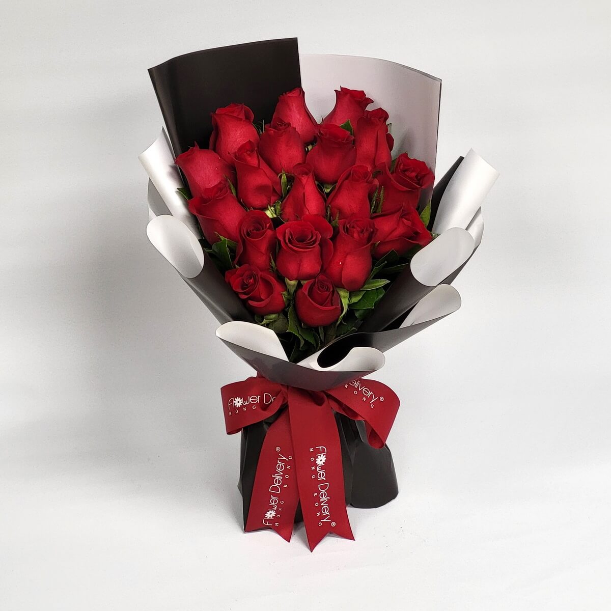Hand-tied bouquet featuring red roses and greenery in black and white wrap 紅玫瑰花束搭配綠葉設計,手綁風格配以黑白色包裝紙,紅色絲帶束口,造型鮮明大氣。