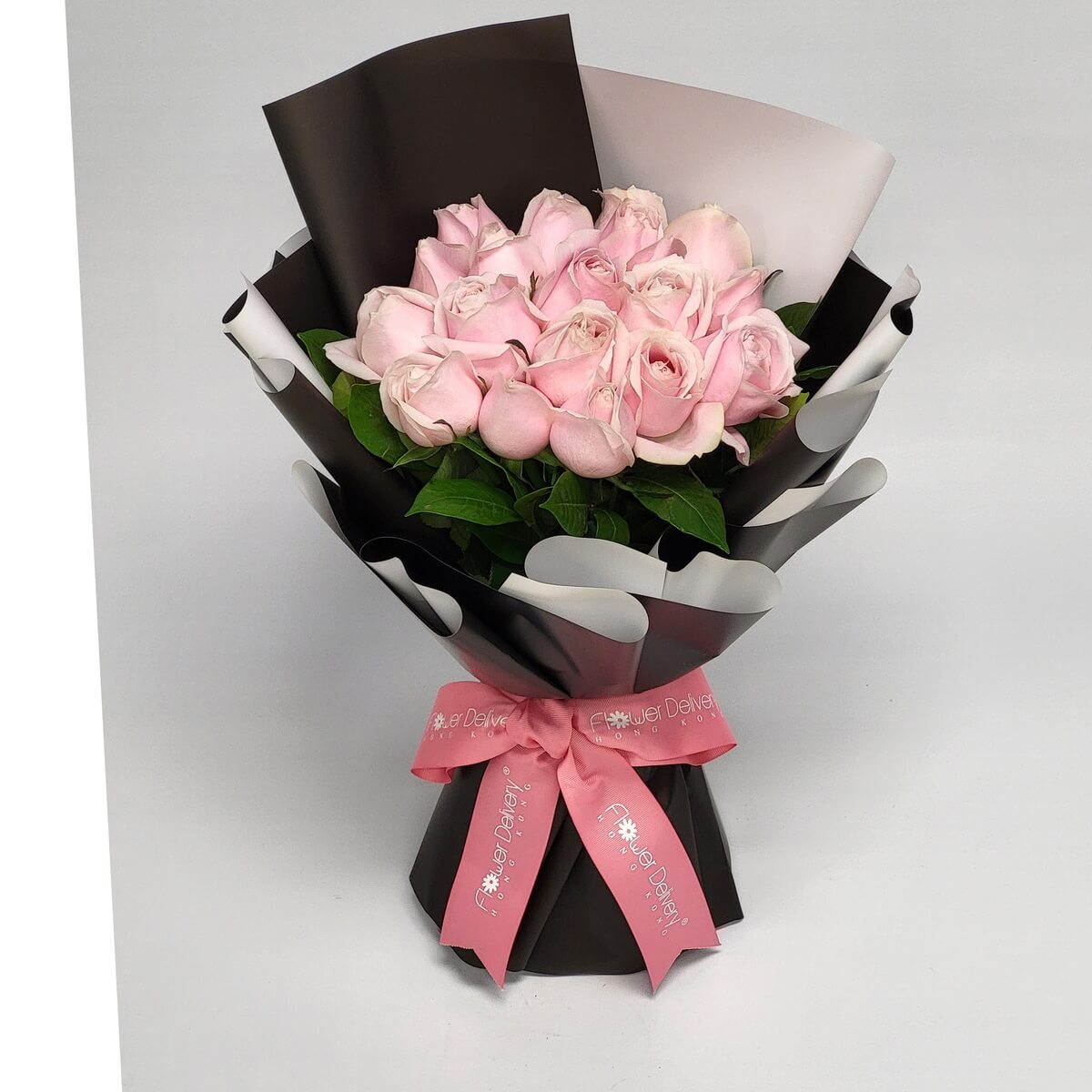 Hand-tied bouquet featuring pale pink roses and greenery wrapped in black and white paper 淡粉玫瑰搭配綠葉設計,手綁花束包以黑白色包裝紙,粉紅絲帶束口,色彩對比柔和典雅。