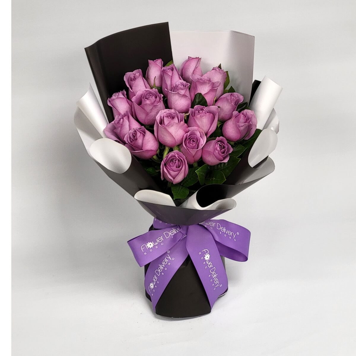Hand-tied bouquet featuring lavender roses and greenery in black and white wrap 淺紫玫瑰花束配搭綠葉,手綁設計使用黑白色包裝紙,紫色絲帶點綴,色調對比鮮明。