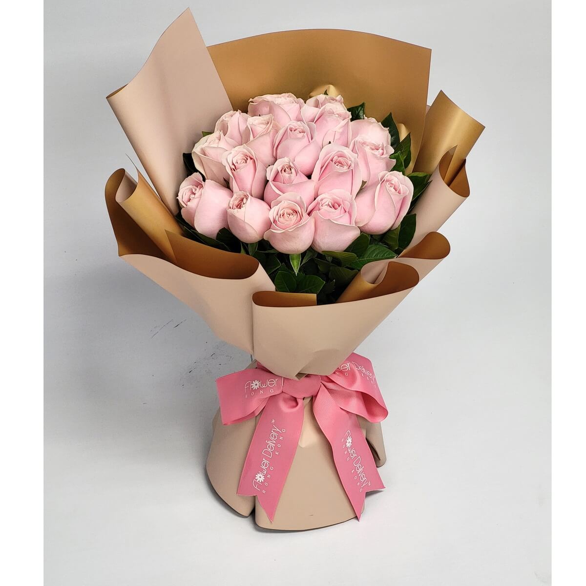 Hand-tied bouquet featuring pale pink roses and greenery, wrapped in champagne and gold paper 淡粉紅玫瑰搭配綠葉,手綁花束設計,以香檳色與金色包裝紙包裹,粉紅絲帶束口。