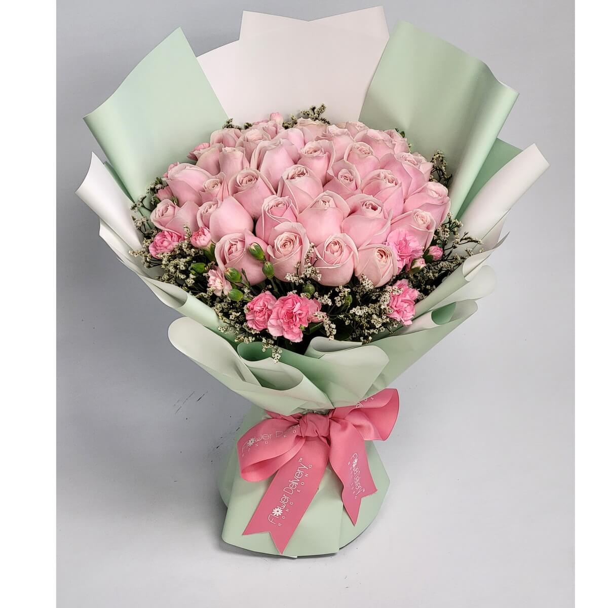 Hand-tied bouquet featuring pale pink roses, mini carnations, and baby's breath 淡粉玫瑰、小粉康乃馨及滿天星搭配,包以柔和淺綠白色包裝紙並以粉紅絲帶束口。