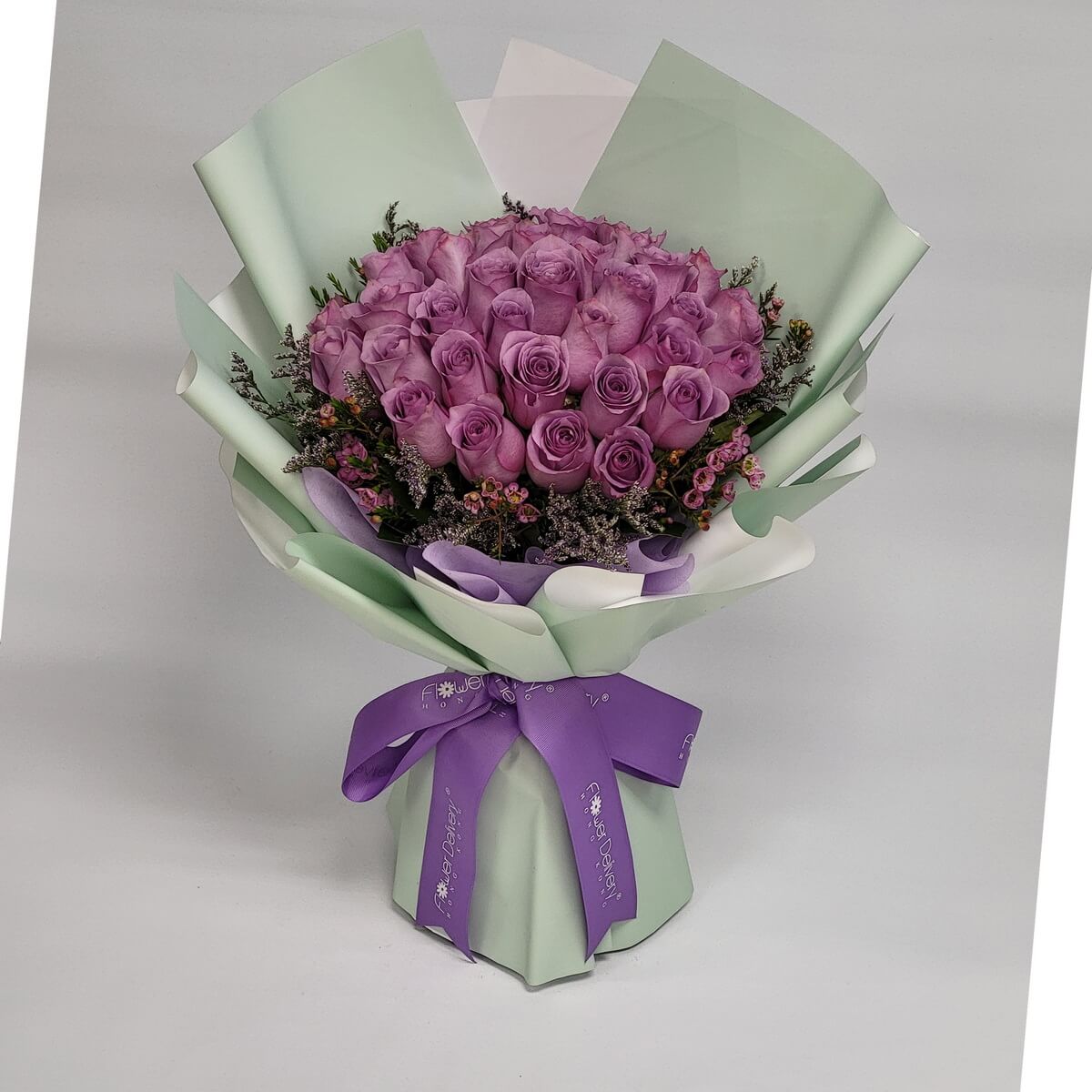 Hand-tied bouquet featuring lavender roses, wax flowers, and caspia wrapped in soft green and white paper 淺紫玫瑰配米花及卡斯比亞花材,包以淺綠與白色包裝紙及紫色絲帶束口。