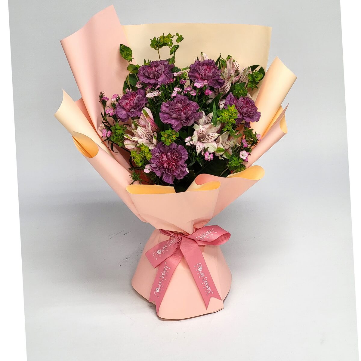 Hand-tied bouquet of purple carnations, pale pink alstroemeria, miniature dianthus, and greenery 紫色康乃馨、粉紅百合草及迷你石竹花配綠葉,包以蜜桃橙包裝紙及粉紅絲帶。