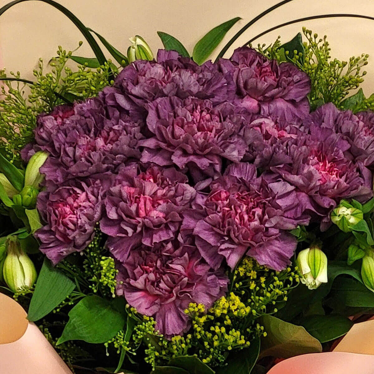 A striking mix of deep purple carnations and green accents wrapped in soft peach tones 濃郁深紫康乃馨與綠色配花交織,蜜桃色包裝增添溫柔氛圍,展現優雅魅力。