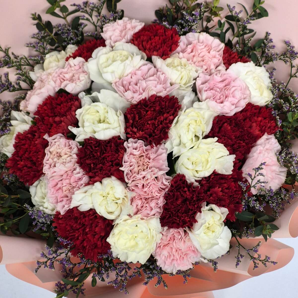 Vibrant Mother's Day bouquet with 36 red, pink, and white carnations, seasonal purple accent flowers and green foliage, wrapped in soft peach and pink paper with red ribbon - 36朵紅色、粉紅色和白色康乃馨母親節花束,配搭季節性紫色點綴花卉和綠色葉材,以柔和桃粉色紙張包裝及紅色絲帶裝飾