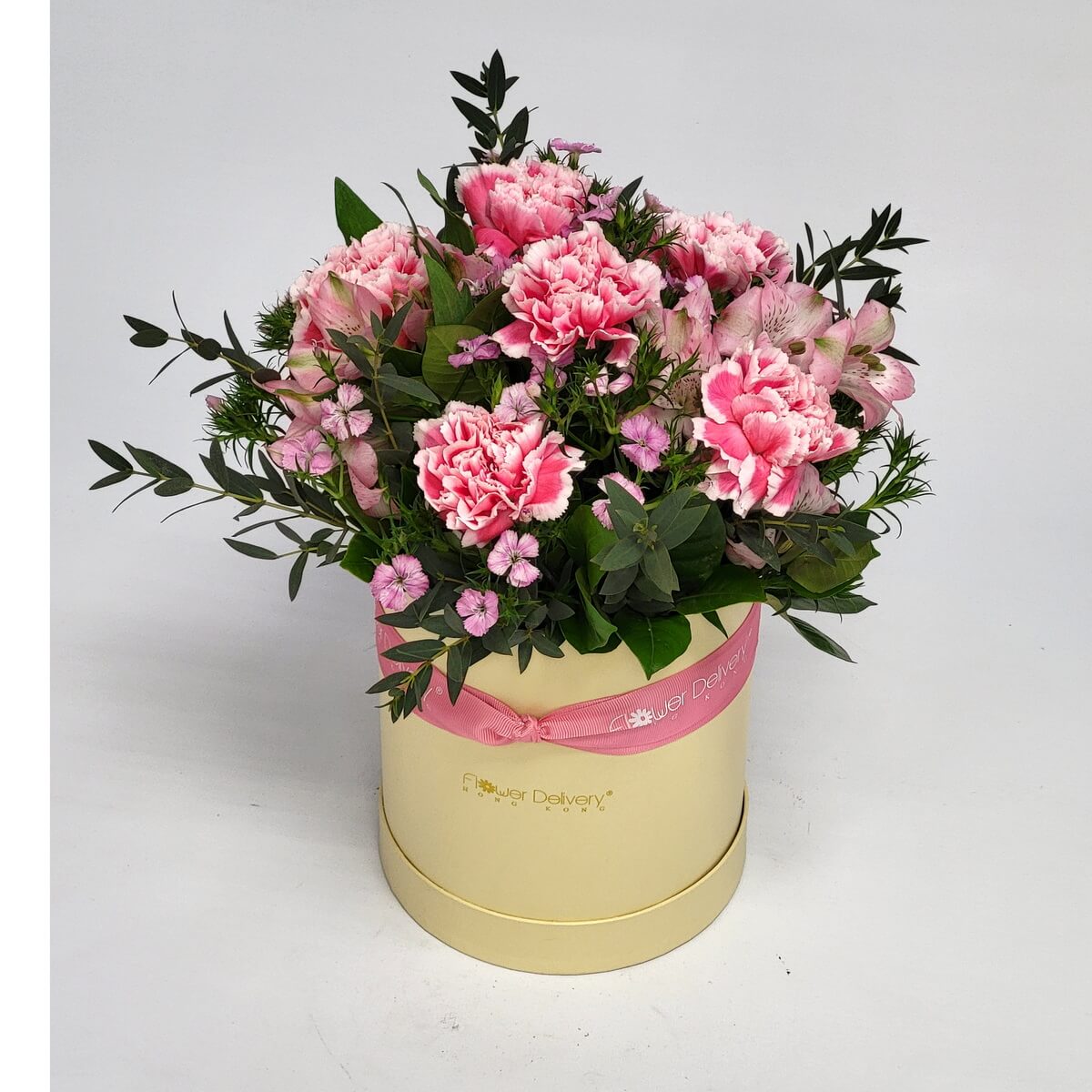Cream round box with pink bi-color carnations, pale alstroemeria, and miniature dianthus 雙色粉紅康乃馨、淡粉百合草及迷你石竹花配上葉材,圓形奶黃色花盒包裝。