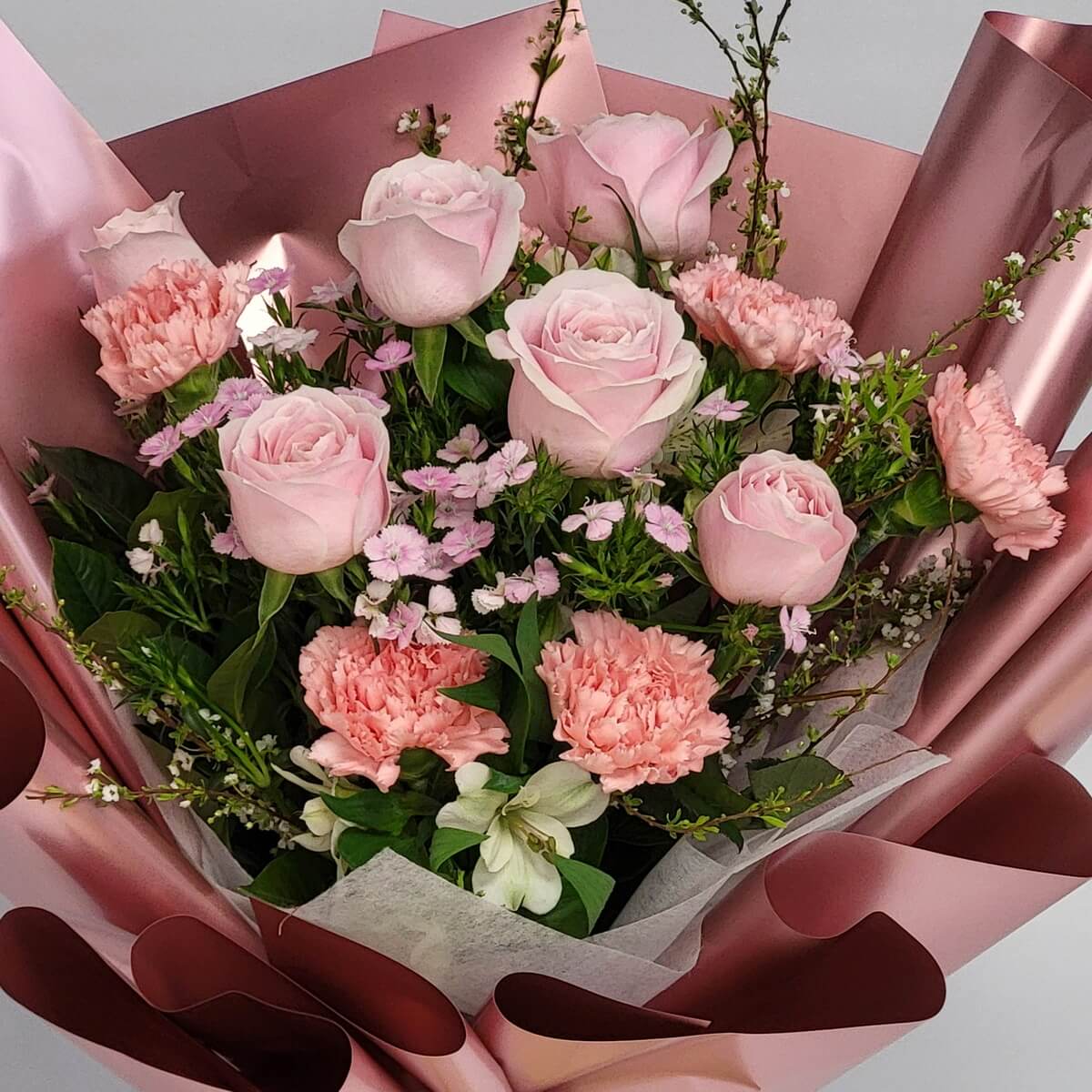 Close-up of blush pink roses and ruffled pink carnations with delicate pink wax flowers, nestled in dusty rose metallic wrapping paper - 淡粉紅玫瑰與皺邊粉紅康乃馨及精緻蠟梅花近距特寫,玫瑰金色包裝紙映襯