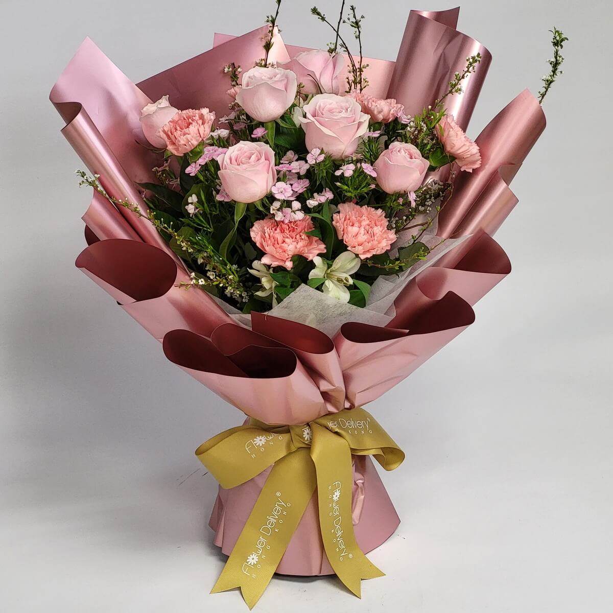 Blush pink roses and pink carnations arranged with layered petals, delicate wax flowers, and white alstroemeria, presented in sculptured dusty rose satin wrapping tied with a gold ribbon - 淡粉紅玫瑰及粉紅康乃馨配層疊花瓣、精緻蠟梅及白色小百合,以立體玫瑰金色緞面包裝繫金色緞帶