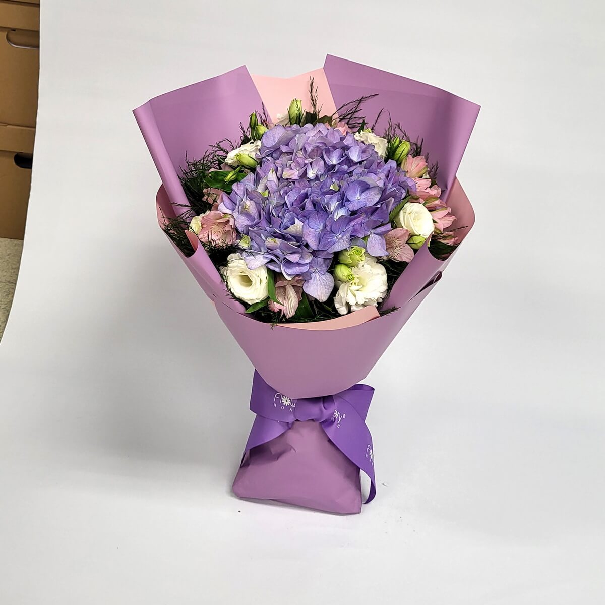 Arrangement of purple hydrangeas with white lisianthus and pink alstroemeria in lavender and blush wrap 紫繡球花、白色洋桔梗及粉紅六出花組成花束,以薰衣草紫及淡粉包裝紙包裹,綁上紫色絲帶。