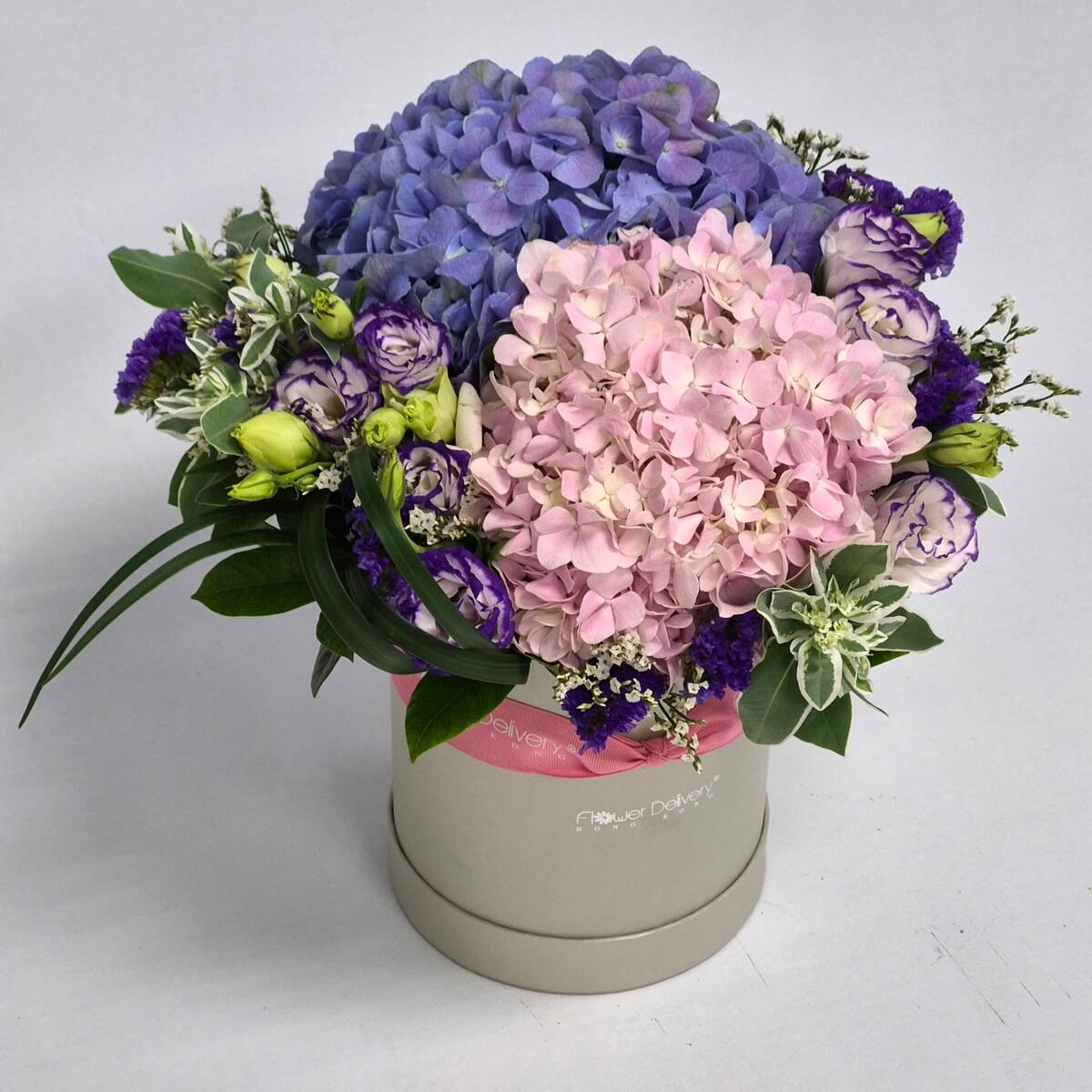 Real photo of Mother's Day flower arrangement in cream round gift box featuring blue and blush pink hydrangeas, white and purple lisianthus, purple statice, green foliage and pink ribbon - 母親節鮮花禮盒,乳霜色圓形禮盒裝,內含藍色及粉紅色繡球花、白色及紫色洋桔梗、紫色補血草及綠色葉材