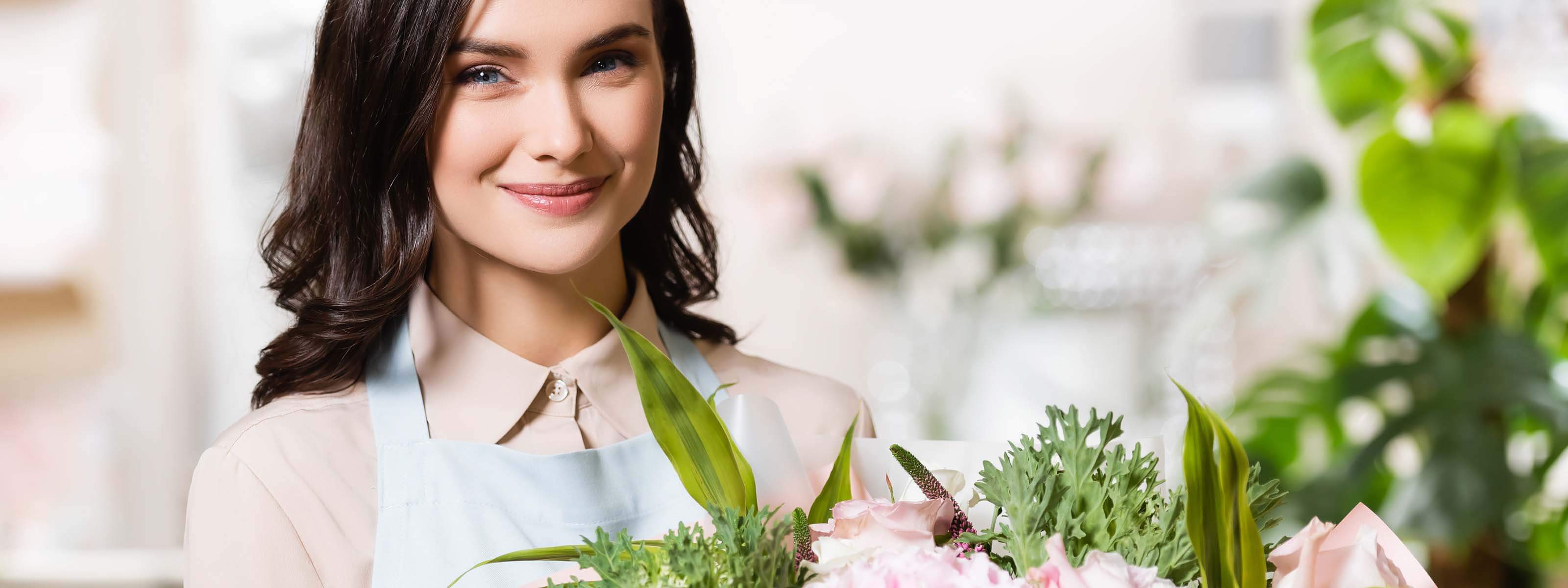 Smiling flower delivery hong kong female florist with neatly arranged pink roses, textured filler and lush foliage in a sunlit flower shop | 微笑的女花藝師,在陽光充足的花店內,手捧整齊排列的粉紅玫瑰,配上富質感的襯花與茂盛綠葉。