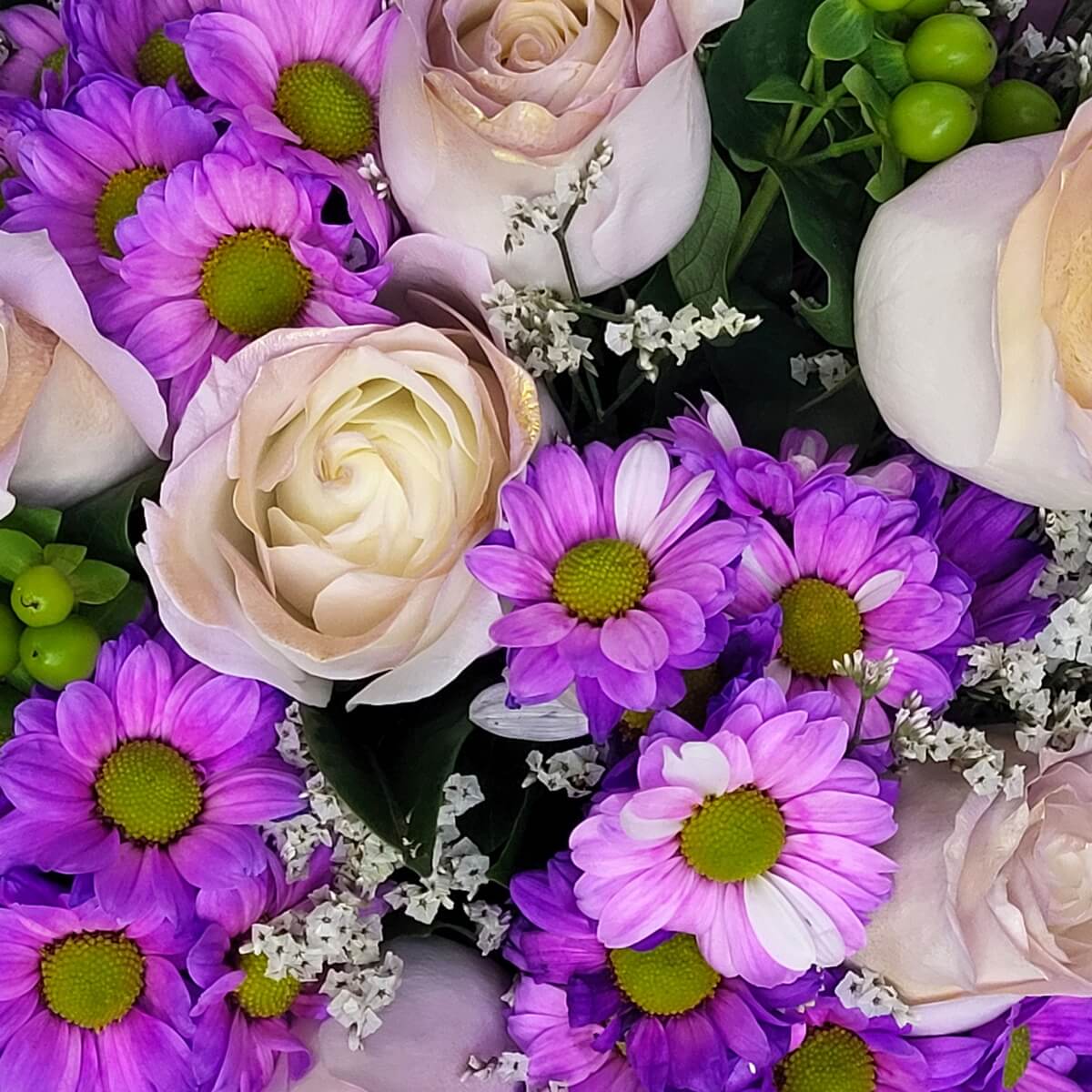 Detail view of cream roses, vibrant purple daisies, green hypericum berries, and white filler blooms | 奶白玫瑰、紫雛菊、綠色鼠尾草果與白色配花組成的花束特寫。