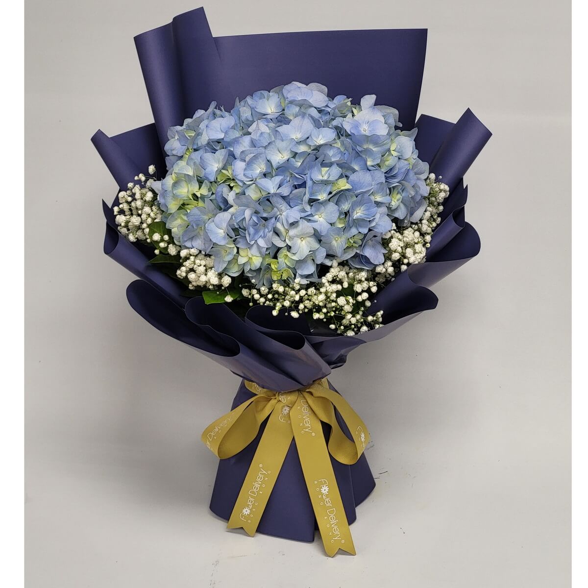 Arrangement of pale blue hydrangeas and baby's breath with greenery, wrapped in navy blue paper and finished with a gold ribbon. 淺藍繡球花與滿天星花束，配綠葉，深藍包裝紙及金色絲帶。