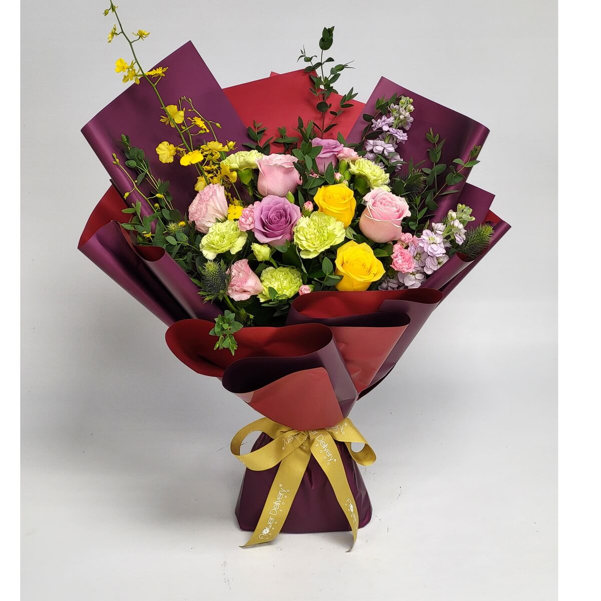 Arrangement of yellow, pink, and lavender roses, green carnations, yellow oncidium, and stock flowers wrapped in burgundy-red paper. 黃、粉紅、紫玫瑰配綠康乃馨、文心蘭及紫羅蘭，酒紅紅色包裝。