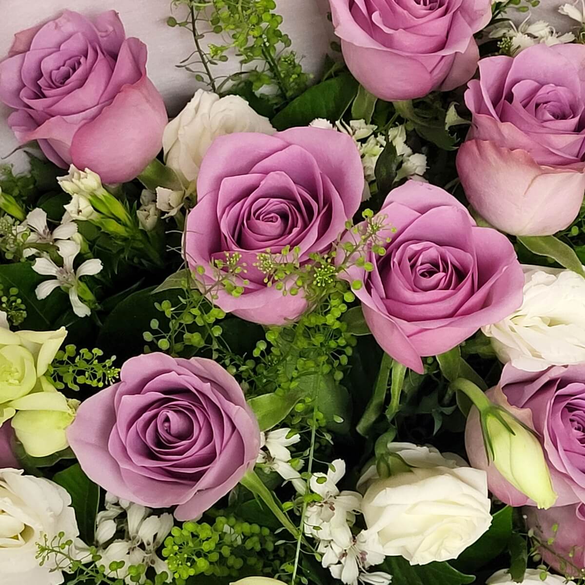 Lavender roses, white roses, and white lisianthus accented by small white filler flowers and lush greenery - 紫玫瑰、白玫瑰及白色洋桔梗配小型白花和茂密綠葉的花藝組合。