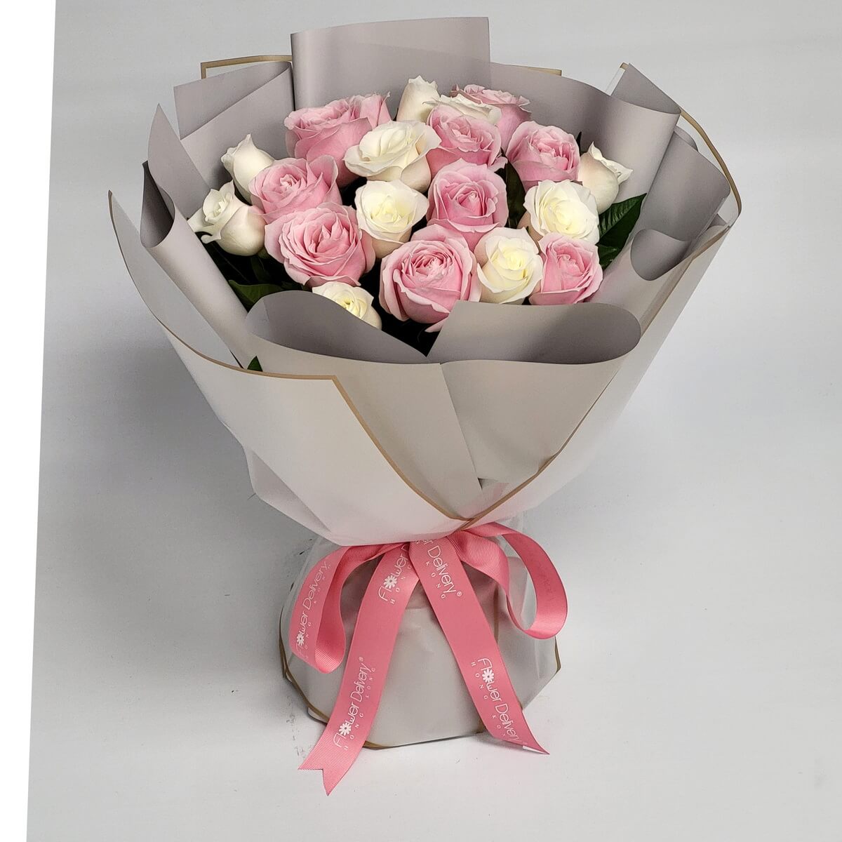 Elegant bouquet of soft pink and creamy white roses wrapped in grey paper with gold trim and pink ribbon. 粉紅與奶白玫瑰花束，灰色金邊包裝，綁上粉紅絲帶。