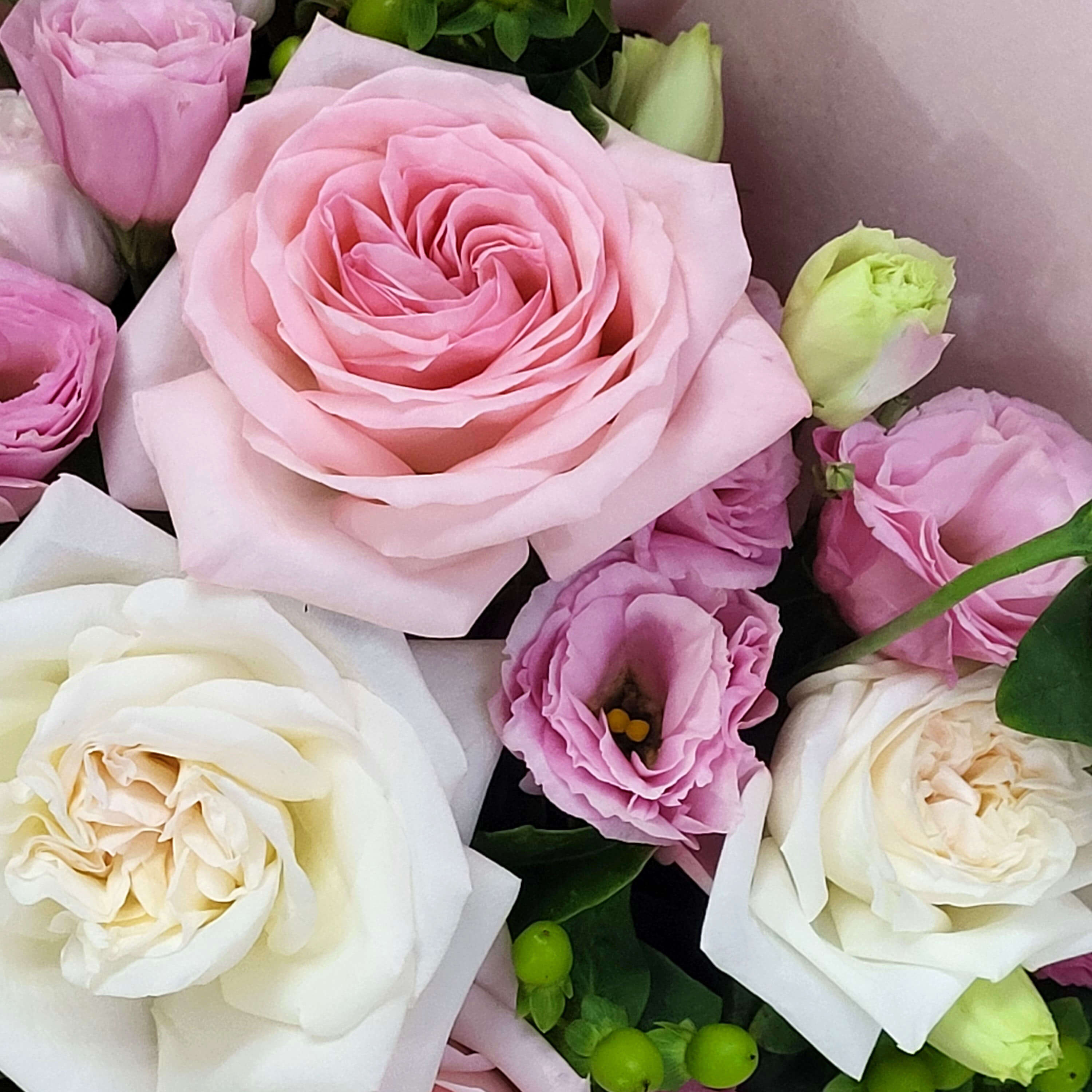 Arrangement of pale pink roses, white garden roses, and light purple lisianthus with green berry accents. | 粉紅玫瑰、白花園玫瑰與淡紫桔梗，加上綠色漿果點綴。