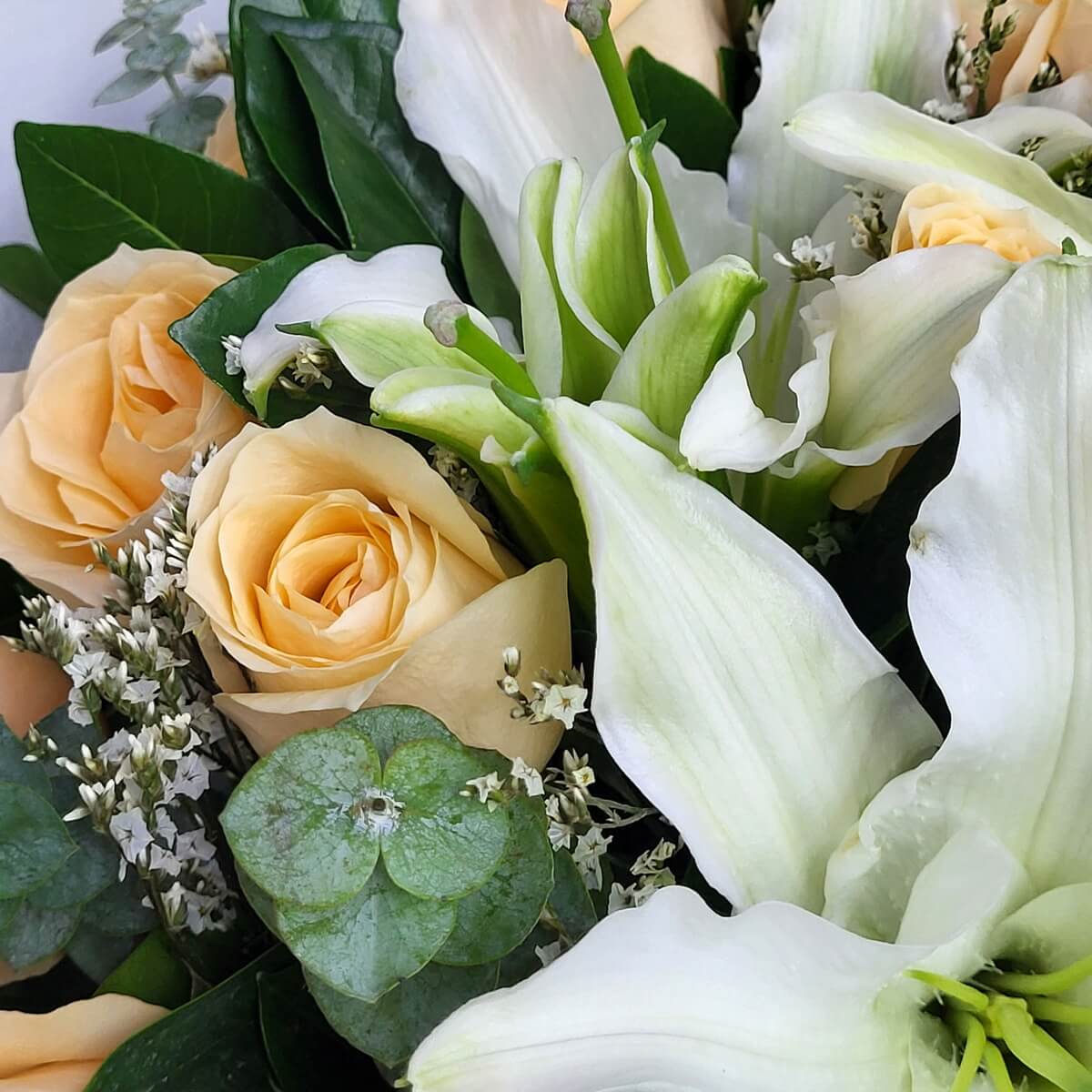 Close-up of white lilies, champagne roses, statice flowers, and eucalyptus 白色百合花與香檳玫瑰特寫，配以白色星狀花材與圓葉尤加利，綠葉襯托整體層次。